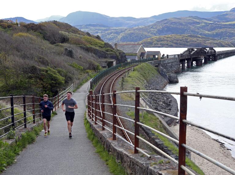 Two joggers running on the path with Barmouth bridge in the background.