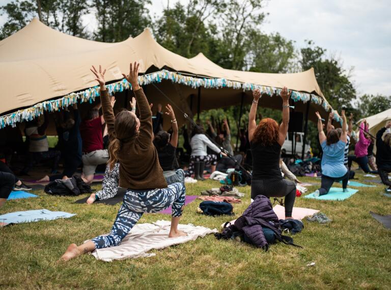 People practicing yoga outside a tent at a festival.
