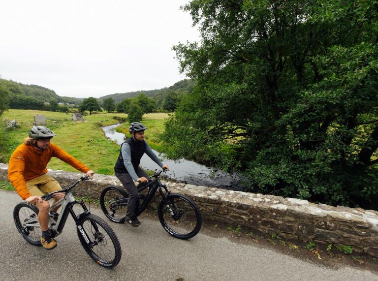 Pair of cyclists cycling alongside a river.