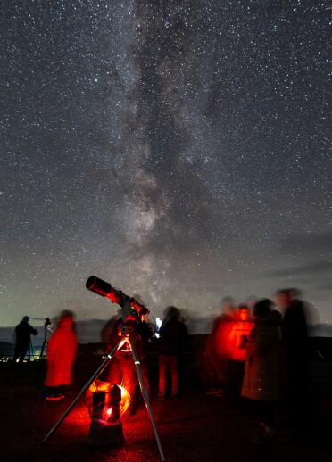Group of people standing by a telescope looking at the night sky.