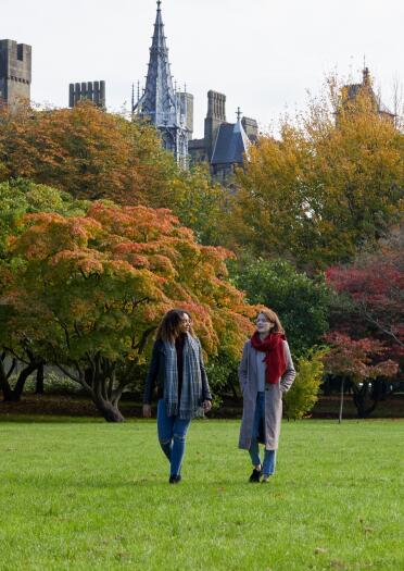 Ladies walking in a park full of autumnal colours with a castle in the background.