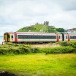 A train travelling alongside the coast and a castle on a hill.
