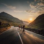 Group of cyclists on a mountain road with the sunsetting beyond.